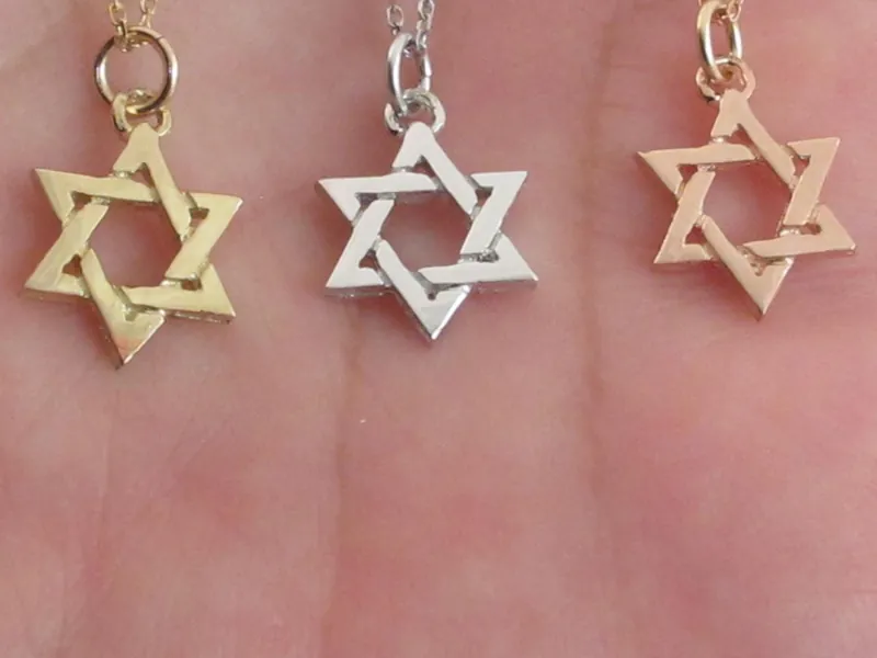 Close-up of three 14k Star of David pendants, in yellow, white and rose gold, resting on a palm